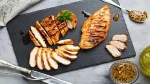 Alimentos para ganhar massa muscular, filé de peito de frango grelhado e fatiado em cima de uma tábua escura