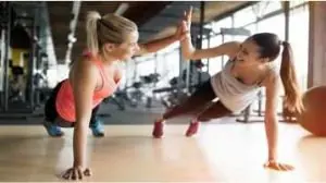 Duas mulheres treinando prancha e batendo na mão uma da outra