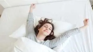 Mulher deitada na cama com lençóis brancos se espreguiçando
