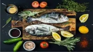 dois peixes em cima da tábua de madeira, cercada por vegetais