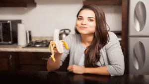 mulher na cozinha comendo uma banana