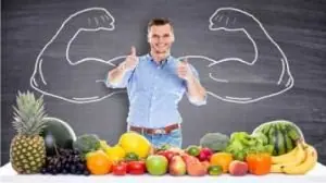 Mesa com frutas e verduras, homem no fundo fazendo sinal de positivo com as duas mãos
