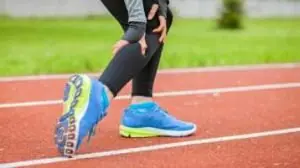 canela de mulher corredora em pista de atletismo, levando a mão à canela por causa de dor