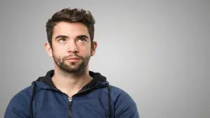 Homem jovem pensando, olhando para cima, fundo cinza