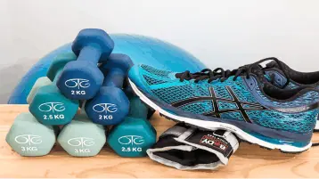Equipamentos de academia azuis, halteres, tênis, tornozeleira e bolo de pilates ao fundo